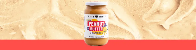 A jar of peanut butter labeled “Peanut Butter Smooth” sits on a red surface, with a creamy peanut butter spread background behind it.