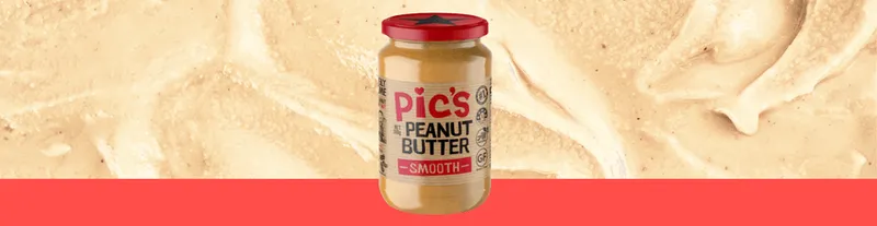 A jar of Pic’s Smooth Peanut Butter with a red lid is centered on a textured peanut butter background and a red band at the bottom.