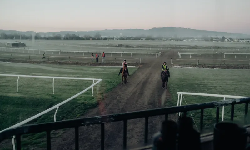 A beautiful sunrise photo from the stands of a racecourse looking out over the track where two horses are being ridden.