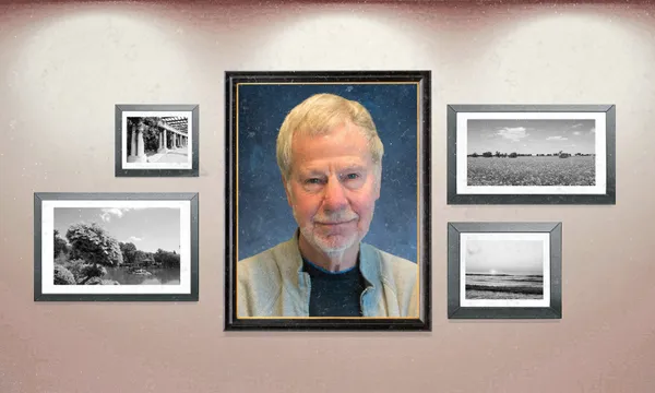 a makeshift photo wall with black and white landscapes and one large school-style portrait of a man with white hair, a white beard and a collared shirt