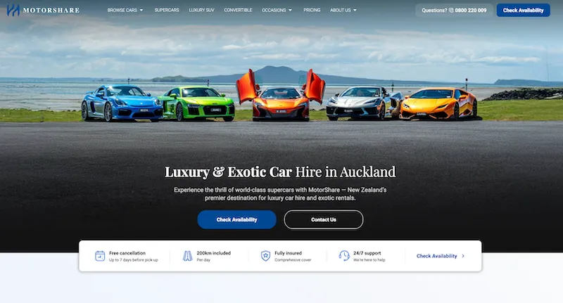 Five luxury sports cars, including models in blue, green, red, grey, and orange, are parked side by side outdoors with ocean and mountains in the background, under a cloudy sky. Website overlay offers car hire in Auckland.