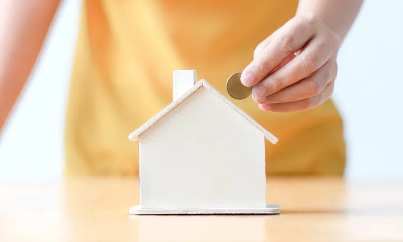 Close-Up Of Hand Holding Coin By Model House