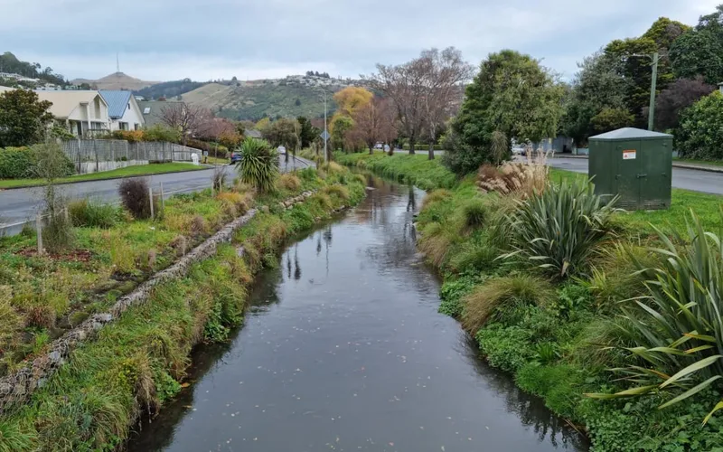 small river with grassy banks between two roads with hills in distance
