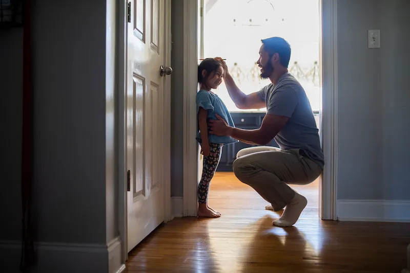Father measuring daughter's height against wall