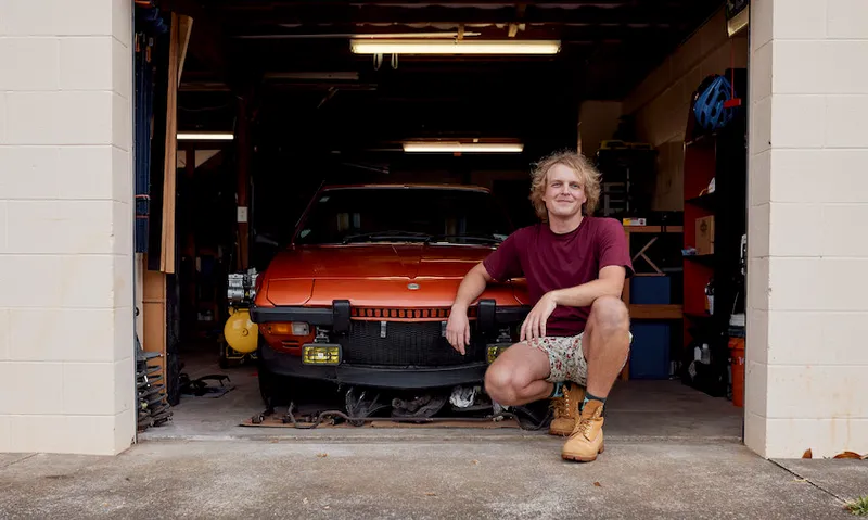 Isaac Grigor outside his four car garage poses with a red car parked just inside.
