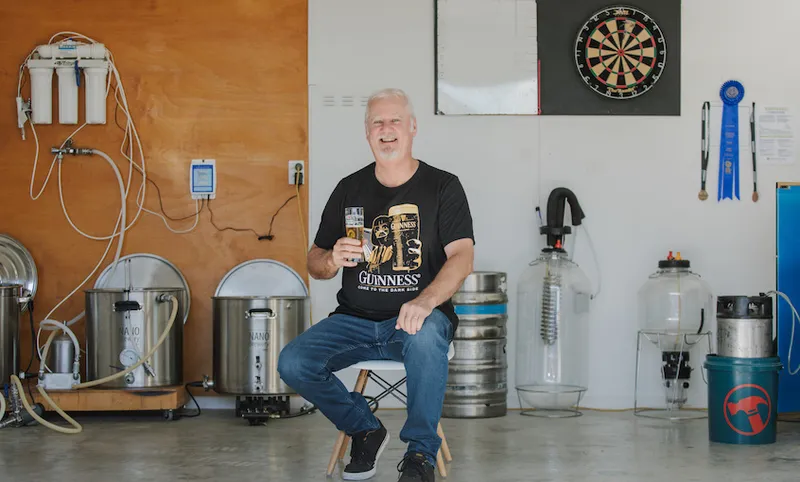 Craig Herron sits on a stool in his garage surrounded by home brew equipment.