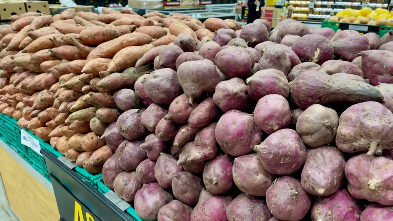 Neatly stacked mounds of red and orange sweet potatoes at a supermarket in New Zealand
