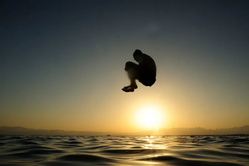 Man jumping into the sea at sunset