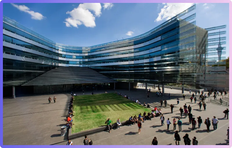 Sir Owen G. Glenn Building: A wide-angle view of the Sir Owen G. Glenn Building, showcasing its modern glass facade and the courtyard with people gathered and walking.