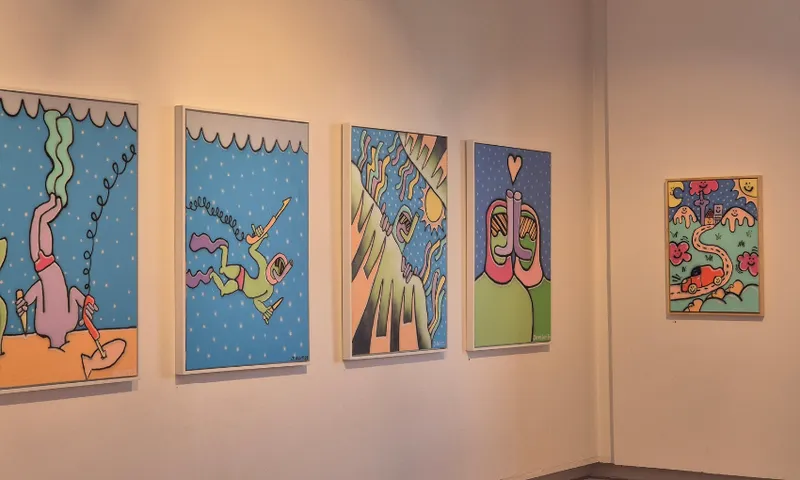 Five colourful, whimsical paintings featuring abstract, cartoon-like characters and playful shapes are displayed on a white gallery wall, illuminated by soft lighting.