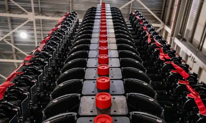 An image in a warehouse shows a stack of satellites all stacked up ready to be loaded into a rocket. The stacked up satellites fit together nicely and compactly, are black with red knobs on them.