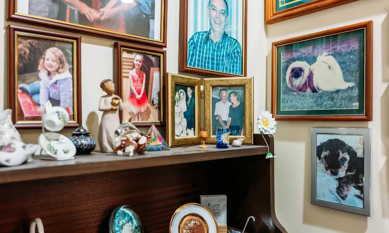 A wooden shelf with decorative items sits below a wall filled with framed family photos, including children, adults, and pets, creating a cozy, personal display.