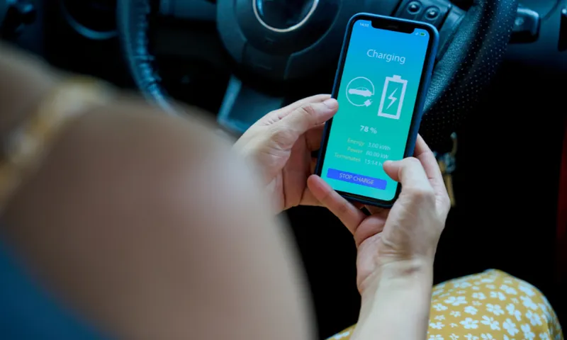 A person in a car holds a smartphone showing an electric vehicle charging app, displaying 78% charge, energy usage, power, and estimated time remaining.