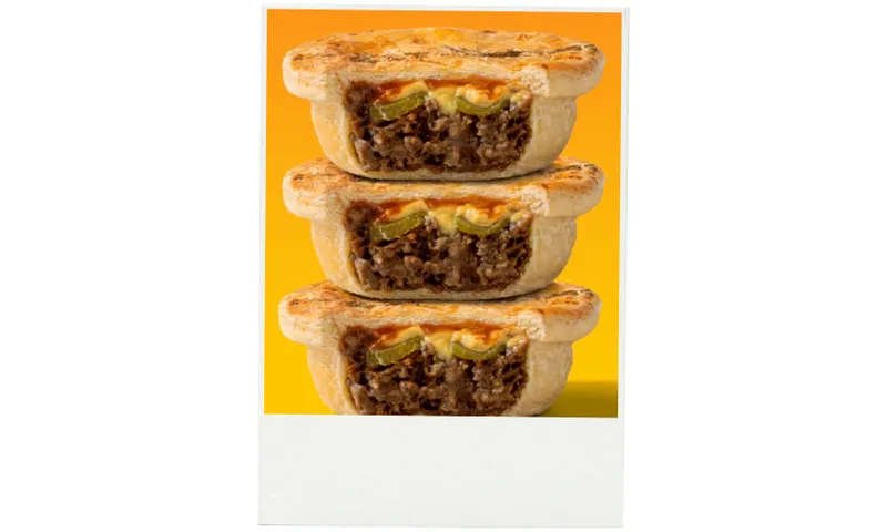 Three beef pies are stacked on top of each other, each cut in half to show the filling of minced beef, cheese, and pickle inside. The background is a gradient of yellow and orange.