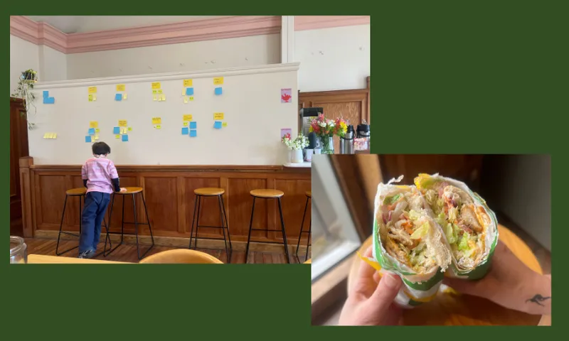 A child stands at a counter covered in sticky notes on a wall in a cozy cafe; next to it, a close-up of a hand holding a halved, loaded wrap sandwich.