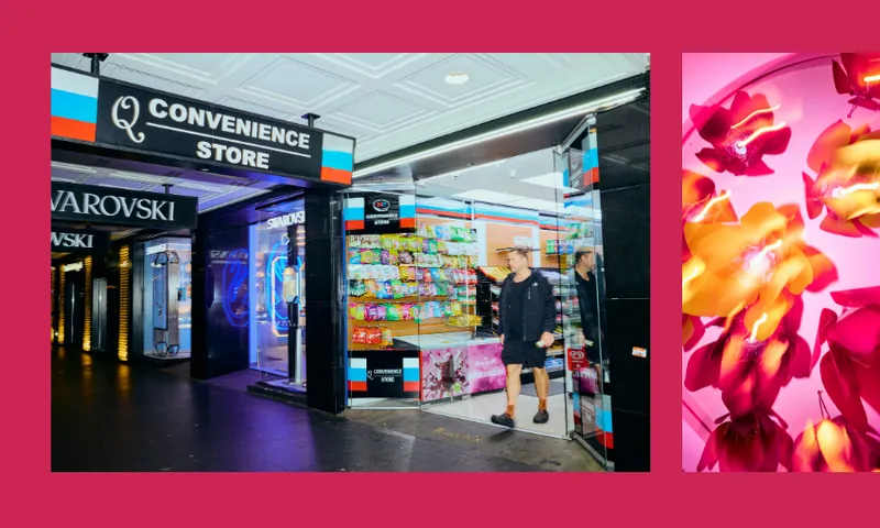 A man stands at the entrance of a brightly lit convenience store next to colorful snacks, with another shop and neon lights visible nearby. On the right, there is a close-up of vibrant yellow and pink flowers.