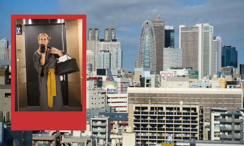 A cityscape of modern skyscrapers and buildings under a blue sky is shown. Overlaid on the left is a red-framed photo of a person in a mirror taking a selfie in an elevator, wearing a robe with a yellow belt and holding a black bag.