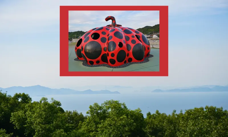 A red pumpkin sculpture with black dots sits on a platform. The sculpture is framed in red and placed over a scenic background of green trees and calm water with distant mountains.