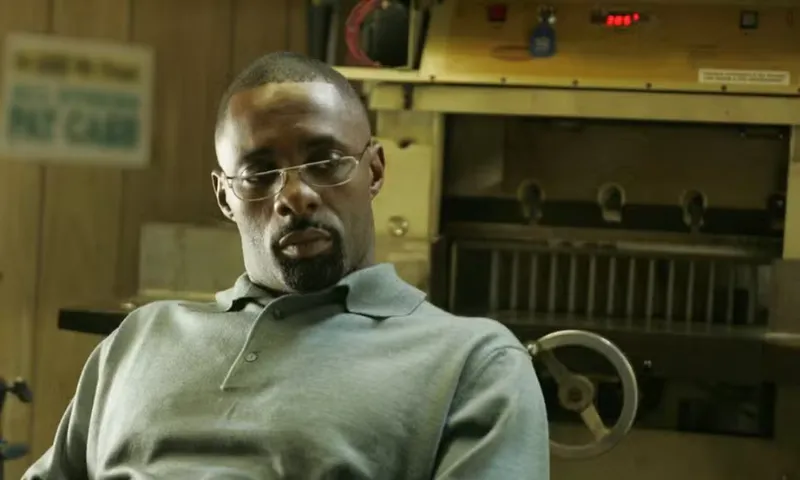 a black man wearing half moon glasses and a polar fleece sits in front of a mantelpiece