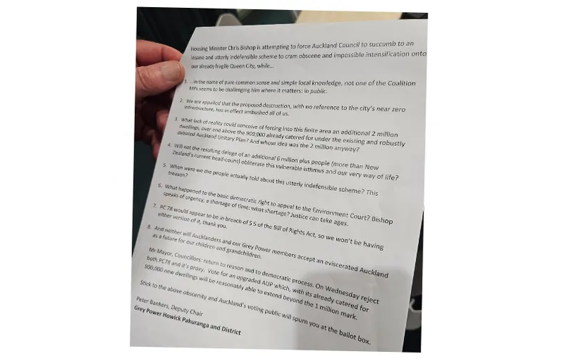 A hand holds a printed document listing concerns about Auckland Council’s housing policy, highlighting issues such as environmental impact, infrastructure strain, and political opposition, with signatures at the bottom.