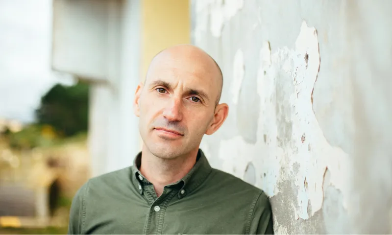 A photo of writer John Summers who is a middle aged man, bald, wearing a green shirt and with an anxious expression.