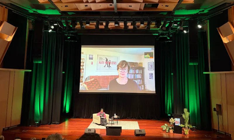 A photo of a stage with a large screen showing the writer Olivia Laing on the screen.