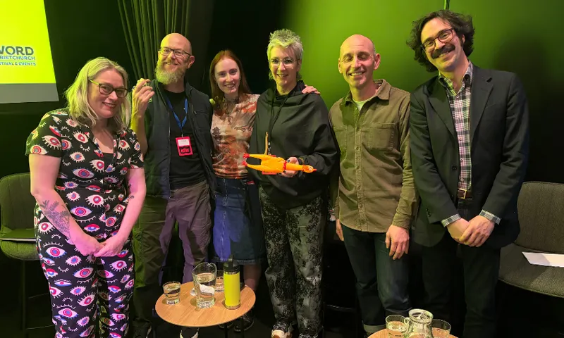 A group of people standing in a semi circle in a dimly lit theatre. All smiling.