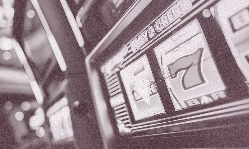 A close-up of a slot machine showing a winning combination with a red number 7 and bar symbol. The image is in a grainy, black-and-white style, with the focus on the reels.