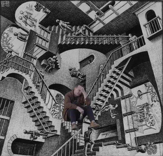 A person sits with their head in their hand, looking stressed, superimposed over M.C. Escher’s artwork “Relativity,” which features impossible staircases and figures walking in various directions.