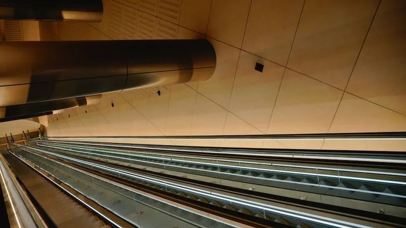 A modern escalator in an indoor space with sleek metal surfaces and geometric wall panels, captured from a unique upward angle.