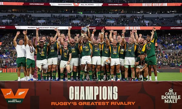 a large rugby team of 30 players wearing green tops and white shorts celebrate with fists raised while standing on a large platform saying "champions"