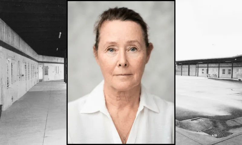 an older woman with white skin, blue eyes and brown hair pulled back in a bun stares sombrely at the camera. In the background a black and white photo of a prison yard