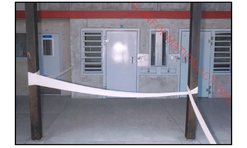 A digital camera photo taken with flash, showing the outside of a cell with a closed door and emergency tape across