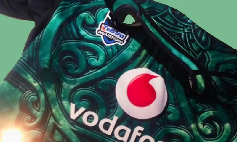 A close-up of a sports jersey with Vodafone and Telstra Premiership logos, featuring a green, swirling pattern with black trim on a pale green background.