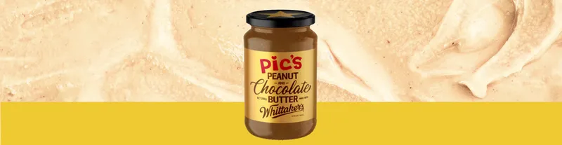 A jar of Pic’s Peanut Chocolate Butter with Whittaker’s sits in front of a creamy, light brown background and a solid yellow strip at the bottom.