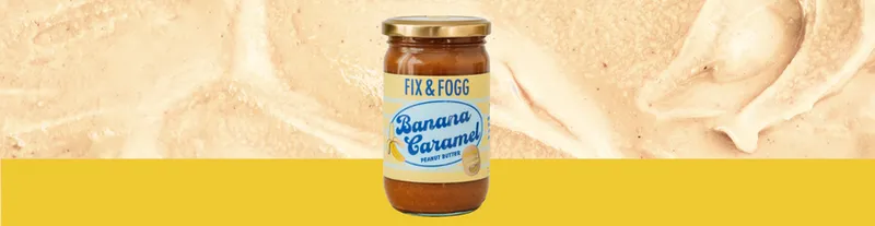A jar of Fix & Fogg Banana Caramel Peanut Butter sits centered on a yellow background with a textured, creamy pattern behind it.