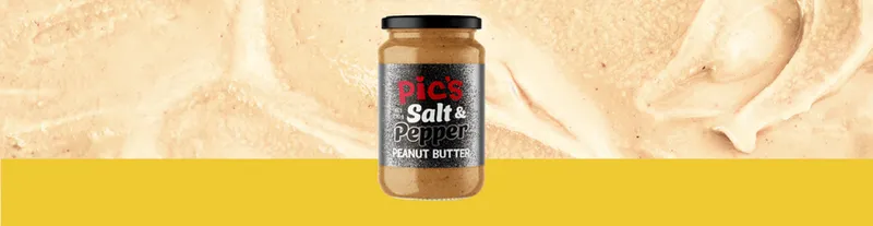 A jar of Pic’s Salt & Pepper Peanut Butter sits centered on a textured peanut butter background with a yellow strip below.