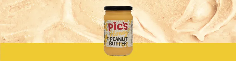 A jar of Pic’s Honey Peanut Butter is centered on a yellow and peanut butter-textured background.