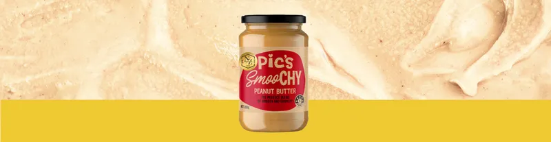 A jar of Pic’s Smooth Peanut Butter is centered on a yellow background with a close-up of creamy peanut butter spread behind it.