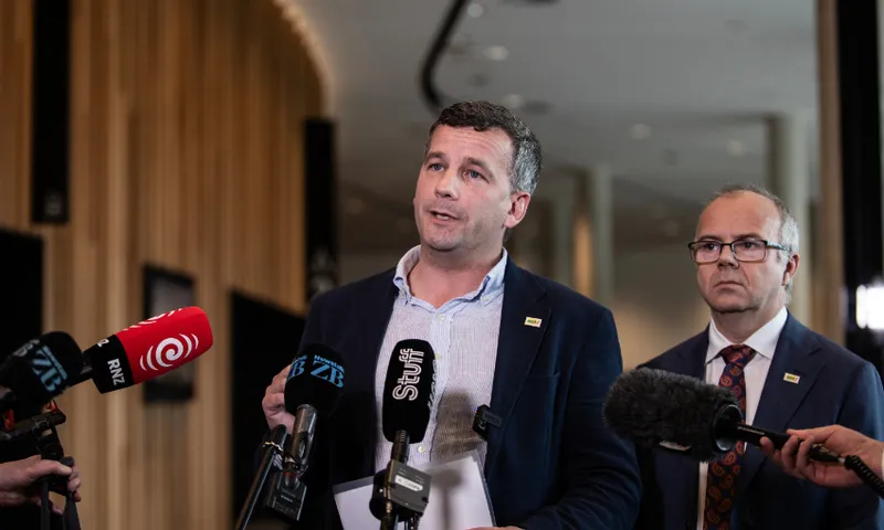 Two men in suits stand in front of press microphones