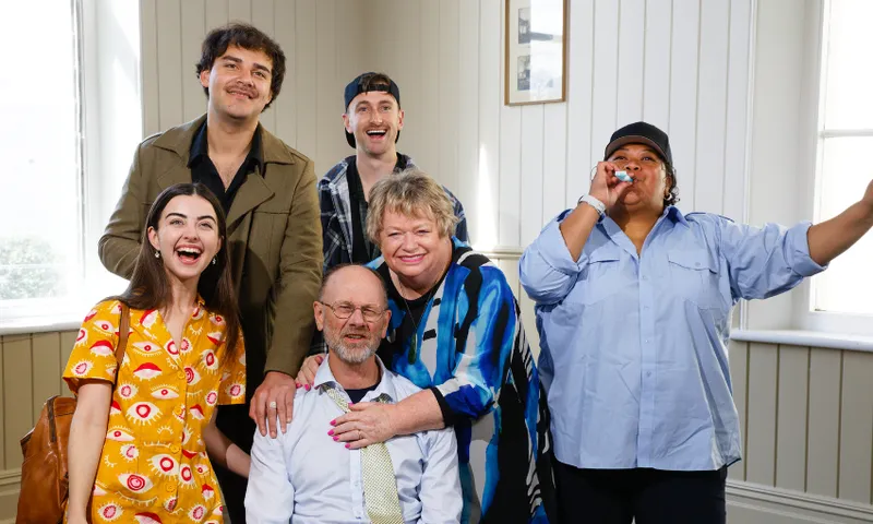 Six people smiling, with one blowing a party blower