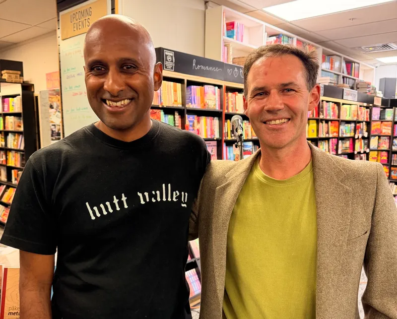 two men smile at the camera while standing in a bookstore