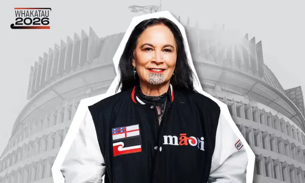 A woman with a chin tattoo smiles, wearing a black and white jacket with Māori symbols. The background shows New Zealand’s Beehive building and a “Whakatau 2026” sign.