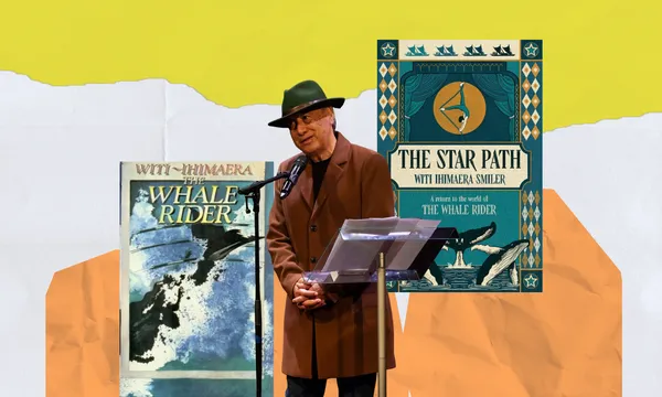 Witi Ihimaera stands to speak at a standing microphone. There's a music stand with paper on it in front of him. He's wearing a hat and brown coat. Behind him are covers of his books The Whale Rider, and The Star Path.