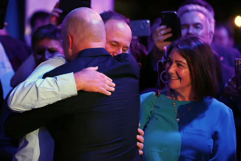 Two men hug as a woman watches on