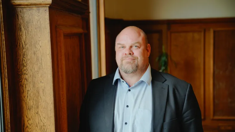 A man wearing a suit jacket looks straight to camera