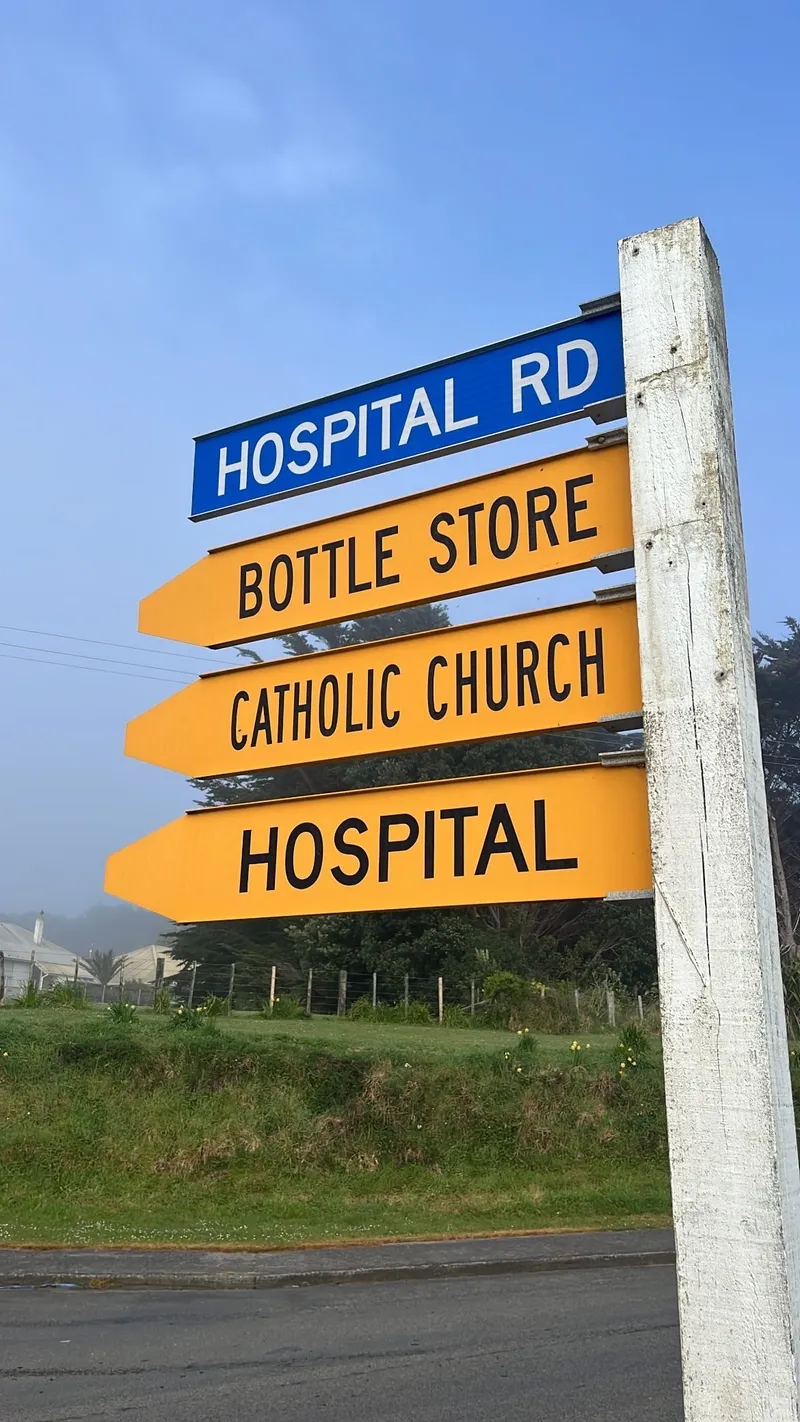 a street sign with yellow tabs signalling hospital road, bottle store, catholic church and hospital