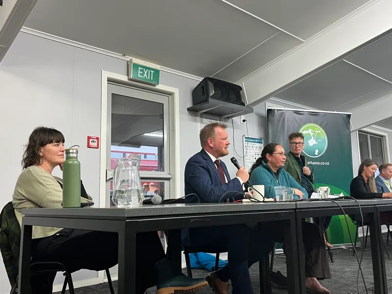 a man speaks into a microphone on a panel, sitting between two women