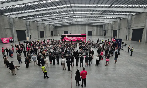 People stand near a pink bus inside an aircraft hangar