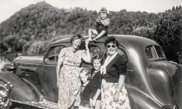 A black and white photo of two women and three children with an old Buick.